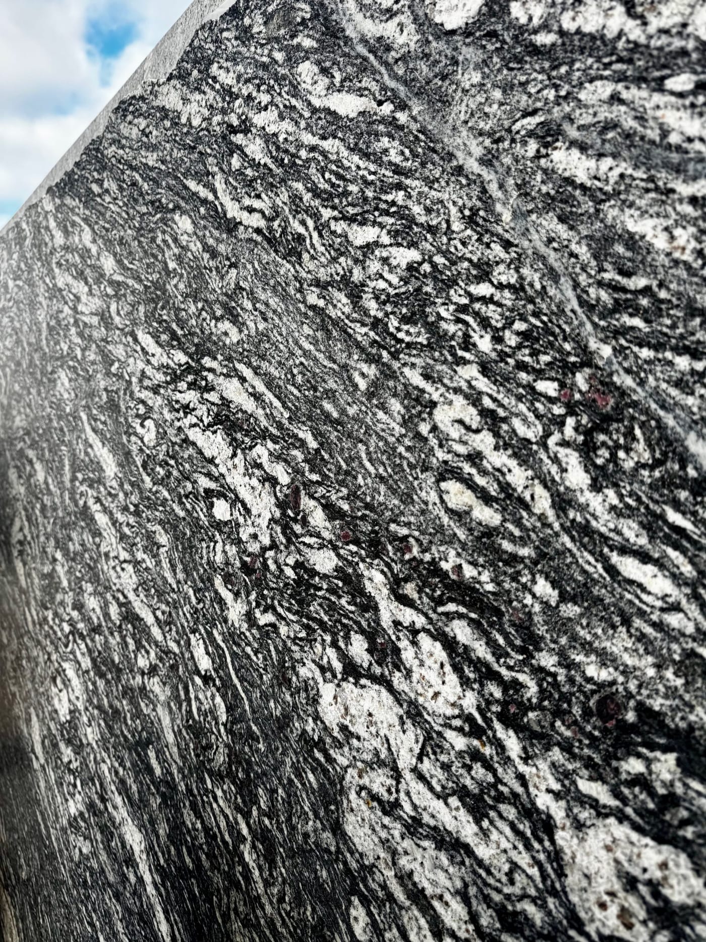 Nahaufnahme einer schwarz-weiß gemaserten Granitoberfläche mit geschwungener Kante vor blauem Himmel.