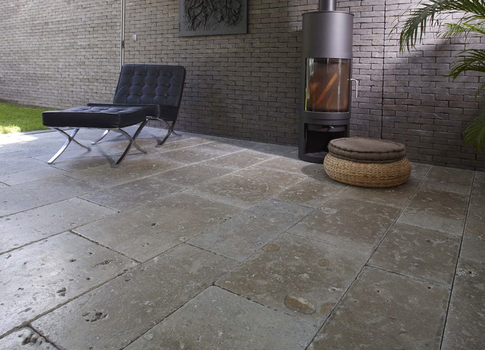 Terrasse mit grossformatigen graubraunen Naturstein-Bodenplatten, Loungesessel und Kaminofen vor Klinkerwand