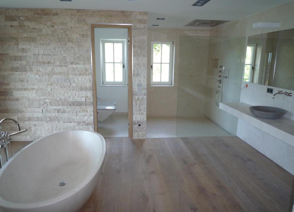 Helles Bad mit Travertin-Bruchsteinwand, freistehender Wanne, offener Dusche und Eichendielen
