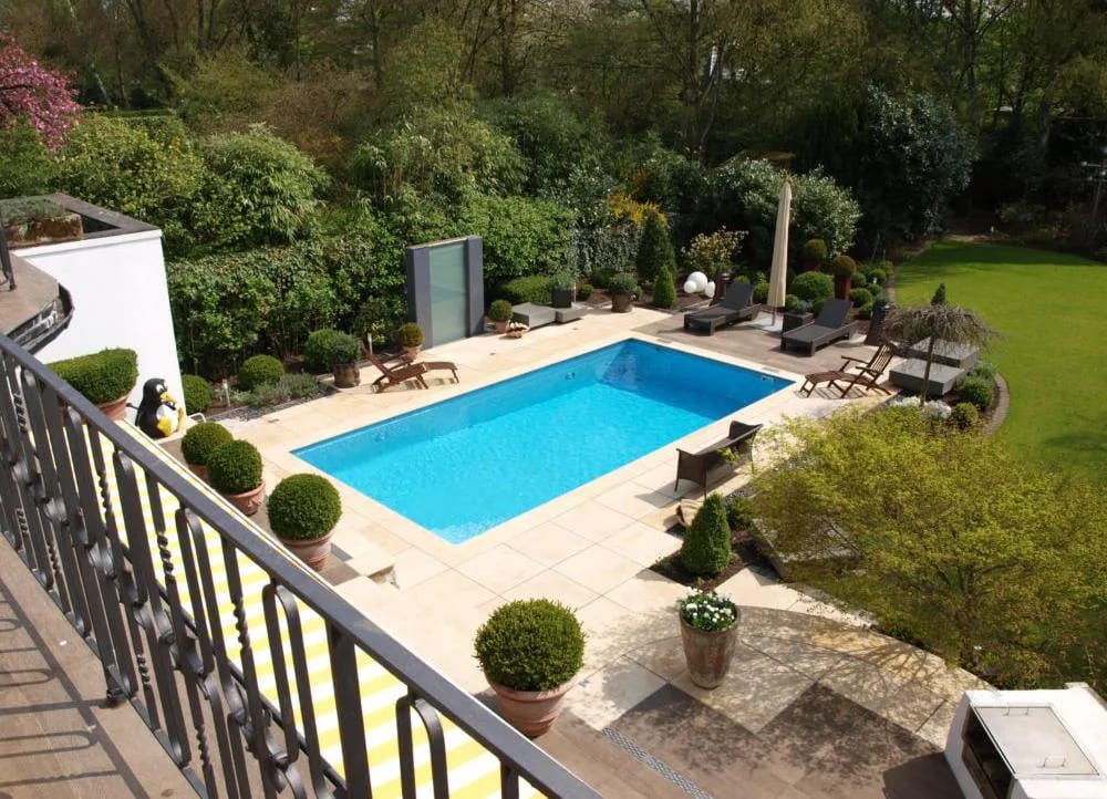 Rechteckiger Pool mit heller Natursteinterrasse, Buchskugeln und Liegen im sonnigen Garten