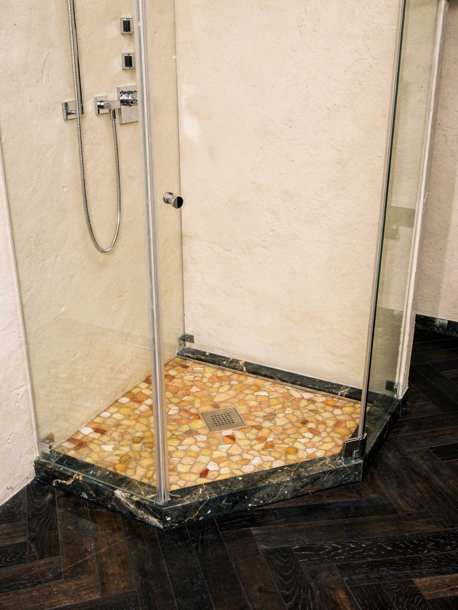 Eck-Duschkabine mit Glasabtrennung, Duschboden aus warmem amberfarbenem Kieselmosaik, dunkler Fischgrät-Holzoptikboden ringsum