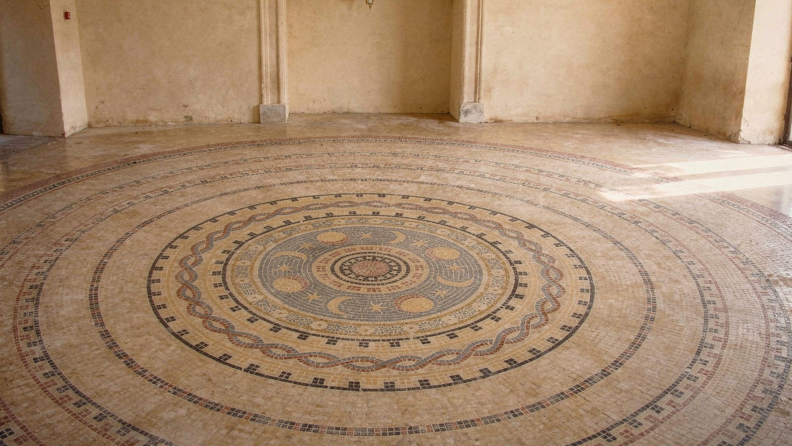 Großes rundes Natursteinmosaik im Boden mit konzentrischen Ornamentbändern und Sonnenmedaillon