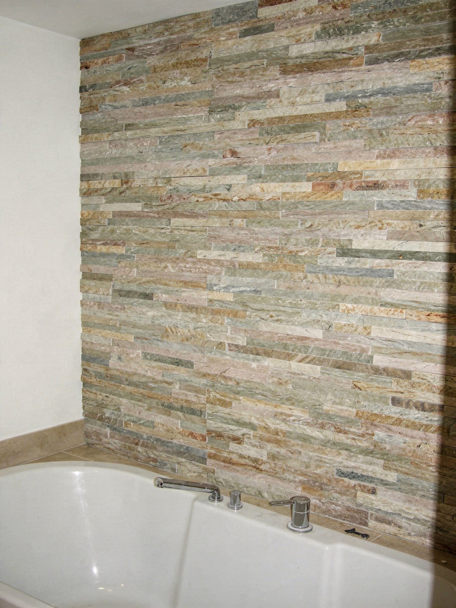 Badezimmerwand mit bruchrauem Naturstein-Verblender in Beige-, Grau- und Rosttönen neben freistehender Wanne