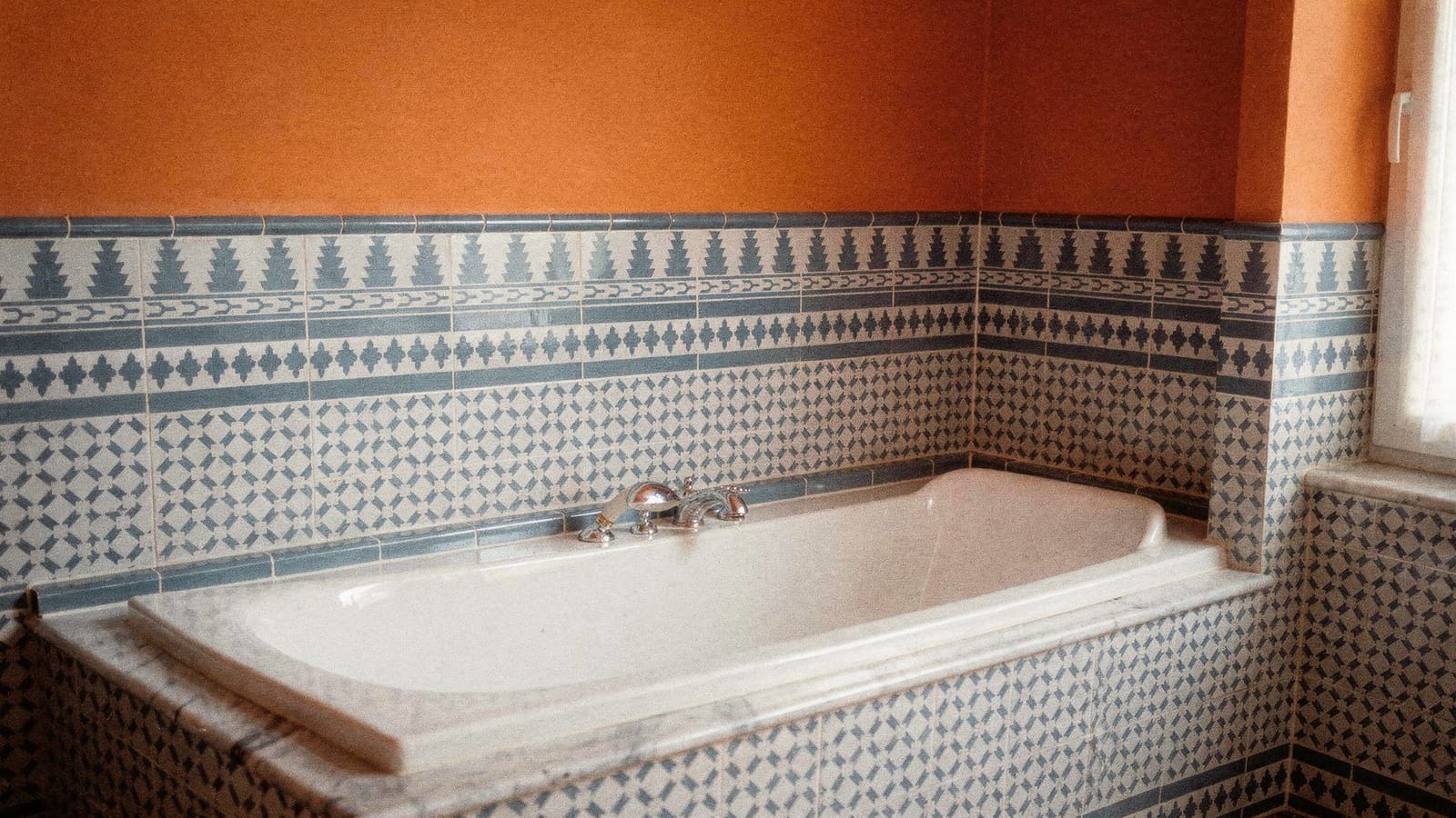 Eingebaute Wanne umrahmt von blau-weißen orientalischen Musterfliesen mit Bordüren, warm getönte Wand