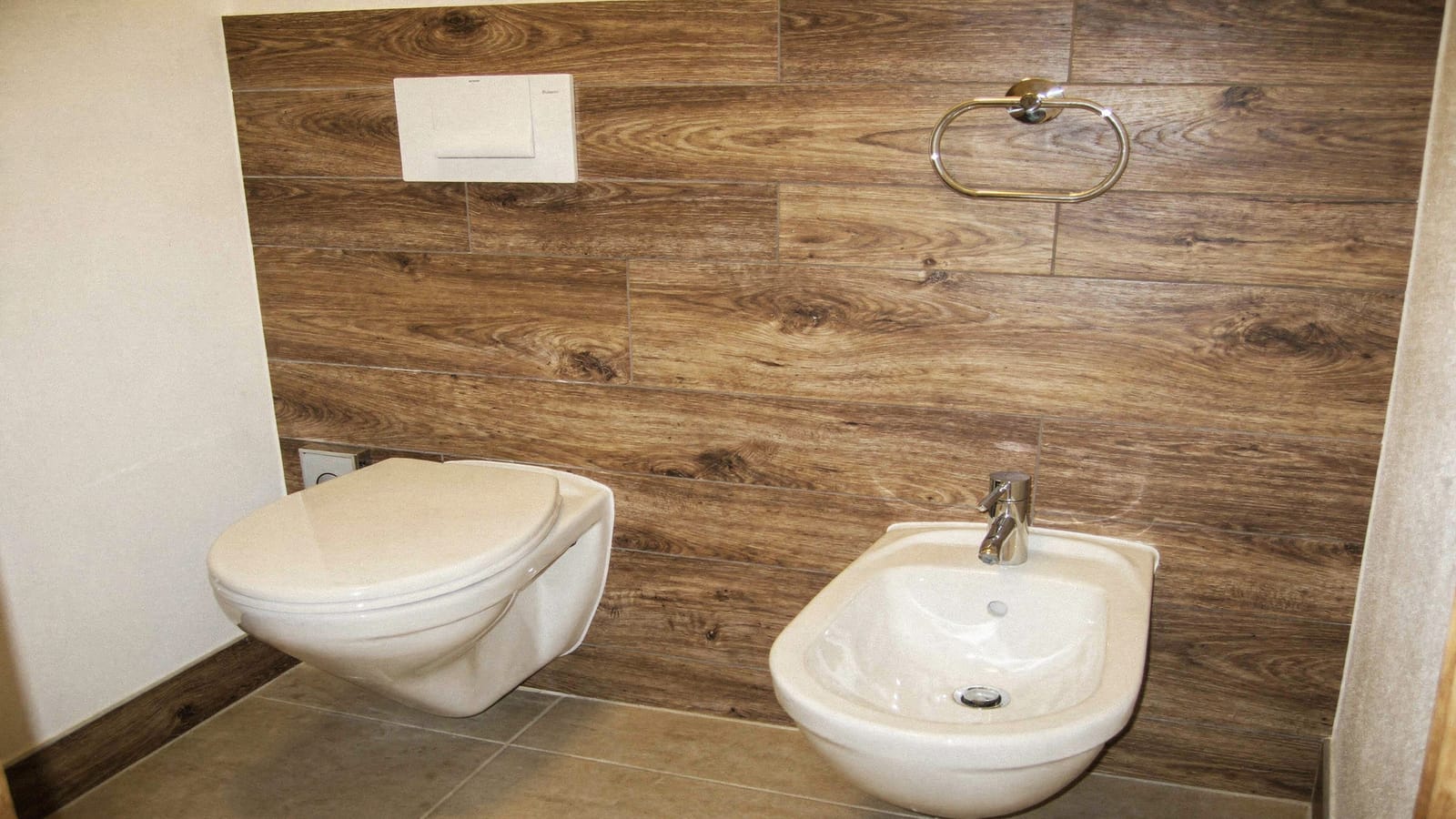 Gaeste-WC mit wandhaengendem WC und Bidet vor braunen Holzoptik-Wandfliesen im Dielenformat