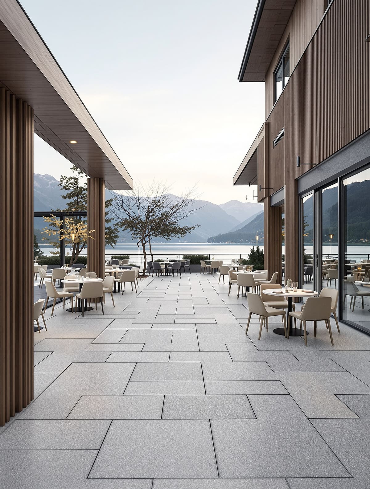 Hotelterrasse am See mit hellem Outdoor-Feinsteinzeug im wilden Verband, gedeckte Tische, Berge im Abendlicht